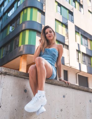 Şehirde oturan kot etekli bir kızın portresi. Arka planda gerçek bir bina var.