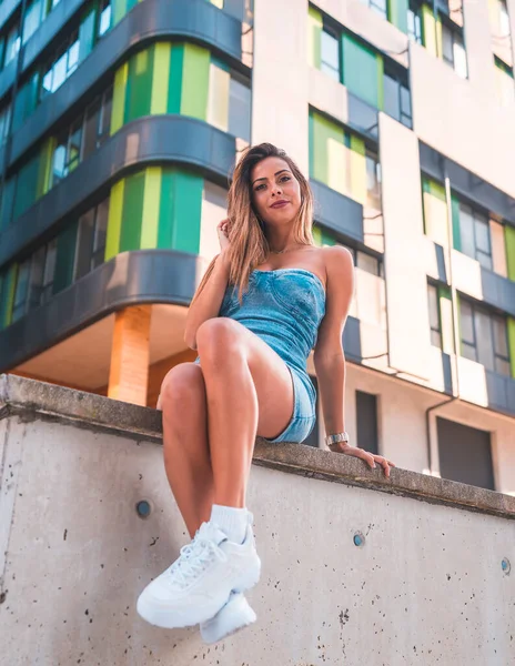 Portrait of a girl in a denim skirt sitting in the city, with a real building in the background