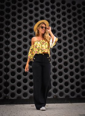 Siyah arka planda şapkalı, dikey fotoğraflı sarı elbiseli sarışın bir kadının portresi.