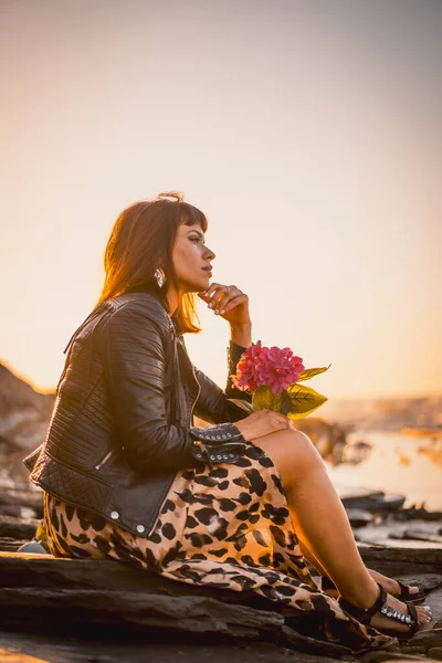 Summer street style on a beach next to rocks of a young brunette caucasian woman in a leopard dress by the sea. Sakoneta beach in the town of Deba, Basque Country. Looking to the right