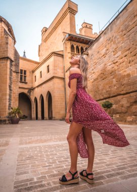 Ortaçağ şatosunda kırmızı elbiseli sarışın bir kadının portresi, yazın tadını çıkarıyor.