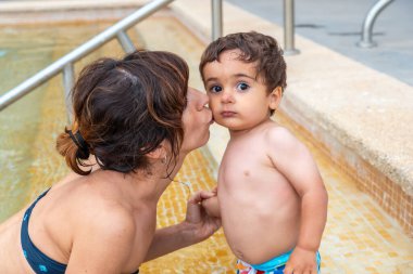 Annesi onu öperken havuzda eğlenen bir bebek.