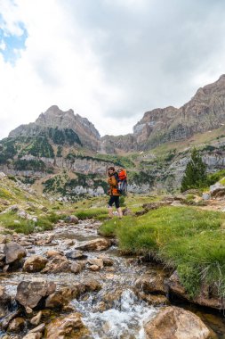 Oğluyla birlikte sırt çantasında gezen bir kadın yaz mevsiminde Pireneler 'de Tena Vadisi' nin yanında yürüyor.