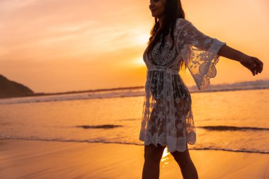 Gün batımında plajda beyaz elbiseli bir kadının silueti yazın tadını çıkarıyor.