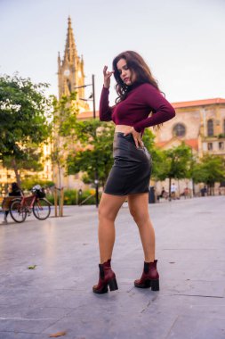 Deri etekli esmer bir kadın şehri ziyaret ediyor, yaşam tarzı, moda pozu, dikey fotoğraf.