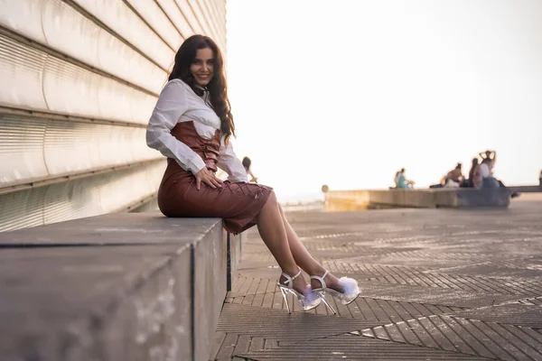 Pretty brunette latin woman in a leather skirt sitting in the city on a sunset