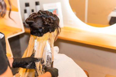 Güzellik salonunda esmer bir kadına sarı boya uygulayan bir kuaförün ayrıntıları.