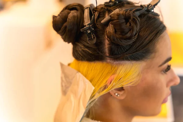 Brunette woman sitting in the beauty salon, hairdresser, applying a blonde dye