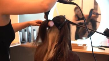 A brunette girl sitting in the beauty salon drying her hair with the dryer, hairdressing