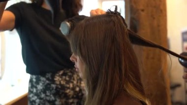 Kurutma makinesi ve kuaförle güzellik salonunda oturan esmer bir kızın portresi.