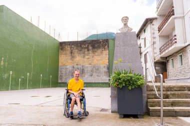 A disabled person in a wheelchair next to a sculpture in the town square