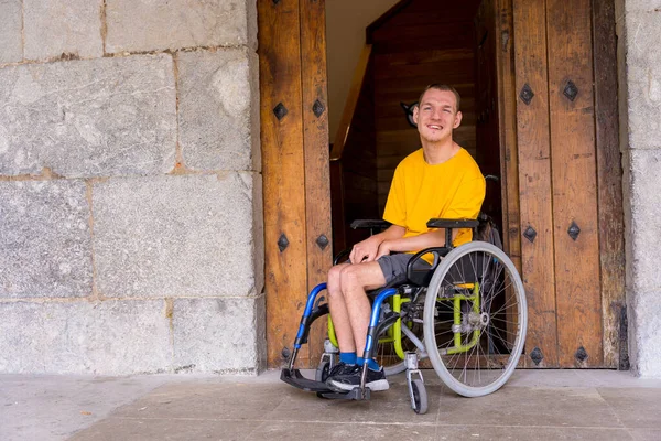 A disabled person in a wheelchair together smiling next to a wooden door