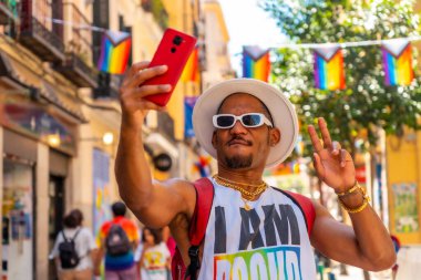 A gay black man at the pride party taking a selfie with the phone, LGBT flag