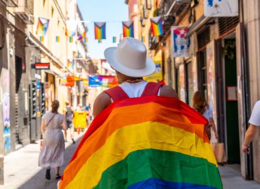 A gay black man walking in the pride party with an LGBT flag, on his back