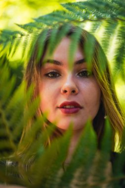 Portrait of a young brunette woman in nature in a natural park with some fern leaves