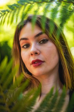 Posing of a young brunette woman in nature in a natural park among fern leaves