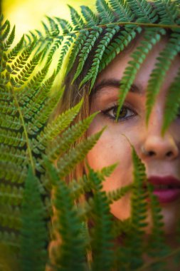Look of a young brunette woman in nature in a natural park among fern leaves