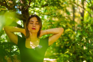 A young brunette woman in nature in the natural park, freedom, dreaming with closed eyes