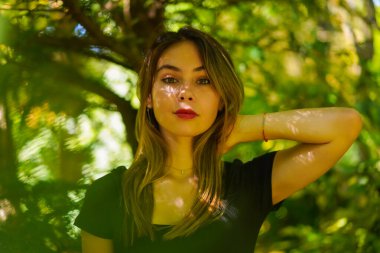 Portrait of a young brunette woman in nature in the natural park, freedom, in the shade of a tree