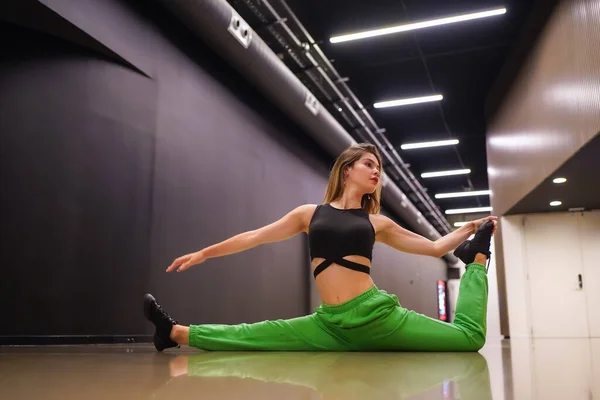 Female urban hip-hop dancer inside a black building building, doing splits in a hallway