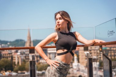 A young model in a viewpoint of the city from the heights, glass railing, looking to the left