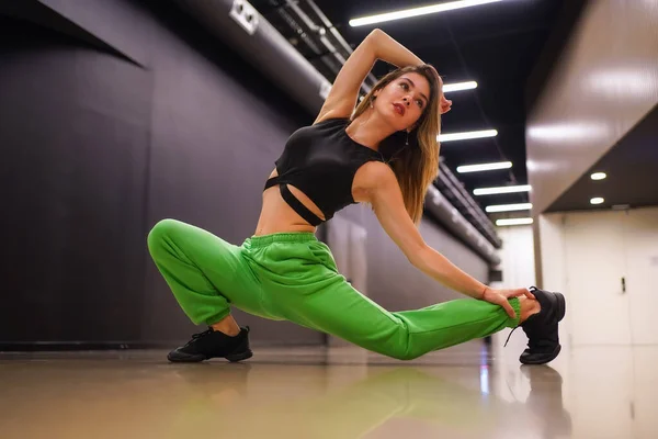 Female urban hip-hop dancer inside a black building building, doing stretching exercises