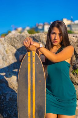 Portrait of a young brunette latin woman with a skateboard wearing a green dress