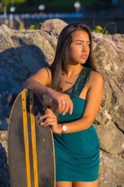 Portrait of a young brunette latin woman with a skateboard on summer vacation