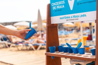 A woman taking an ashtray to smoke on the beach in summer and not throw the ash or the cigarette on the sand