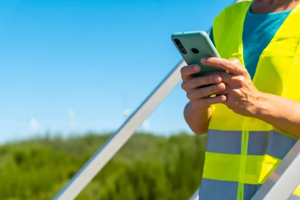 Woman worker in a wind farm, green energy, reviewing the notes with the phone