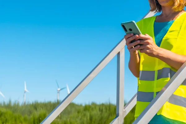 Woman worker in a wind farm, green energy, technical review, with the phone in her hand
