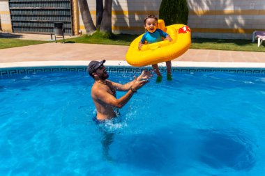 Father playing with his son with a yellow float in the pool in summer, throwing it