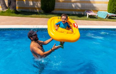 Father playing with his son with a yellow float in the pool in summer, doing jumps