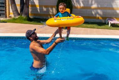 Father playing with his son with a yellow float in the pool in summer, flying