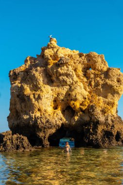 A tourist in the water next to the rocks at Praia dos Arrifes, Algarve beach, Albufeira. Portugal