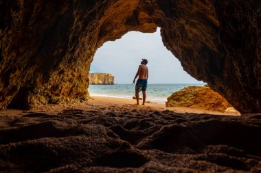 A man in the natural cave in the Algarve in summer on the beach at Praia da Coelha, Albufeira. Portugal