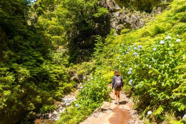 A young woman on the trail next to the waterfall at Levada do Caldeirao Verde, Queimadas, Madeira