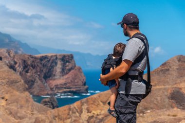 A father with his baby in his backpack in Ponta de Sao Lourenco looking at the landscape and the sea, Madeira