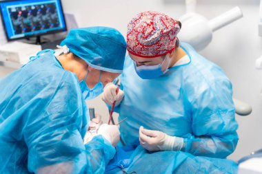 Diş kliniği, dişçi doktoru ve mavi ameliyat asistanı bayan bir müşteriyle çalışıyor.