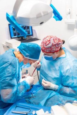 Diş kliniği, dişçi doktoru ve mavi elbiseli asistan bir implant ameliyatı yapıyor.