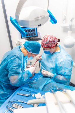 Diş kliniği, dişçi doktoru ve mavi elbiseli asistan bir implant ameliyatı yapıyor.