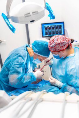 Mavi elbiseli doktorlar hasta üzerinde karmaşık bir ameliyat yapıyorlar, düz aksiyonlu fotoğraf.