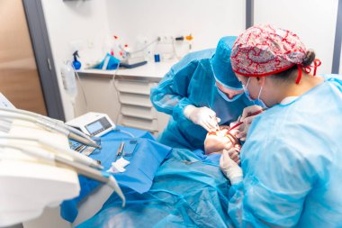 Diş kliniği, mavi elbiseli dişçiler bir implantı ameliyat ediyorlar.