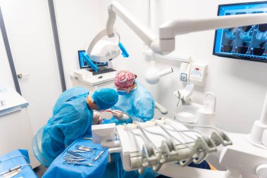 Diş kliniği, mavi elbiseli dişçiler bir implantı ameliyat ediyorlar.