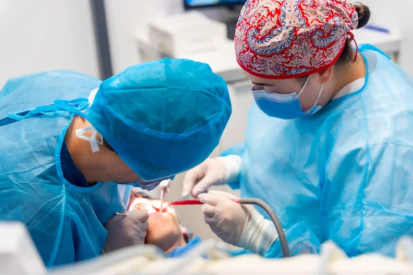 歯科医院 青いスーツの女性歯科医 口腔手術を行う帽子 — ストック写真