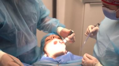 Diş kliniği, dişçi doktoru ve mavi elbiseli asistan bir implant ameliyatı yapıyor.