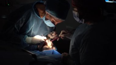 Diş kliniği, dişçi doktoru ve mavi elbiseli asistan bir implant ameliyatı yapıyor.