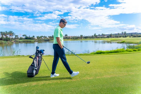 Man playing golf at golf club by a lake, driver, iron, pitching