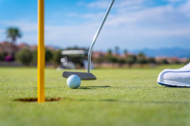 Golf oynayan bir adamın ayrıntıları, golf sopasıyla topu yeşildeki deliğe sokması.