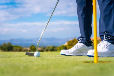 Topu golf sopasıyla yeşildeki deliğe sokuyorum. Golf oynayan adam.